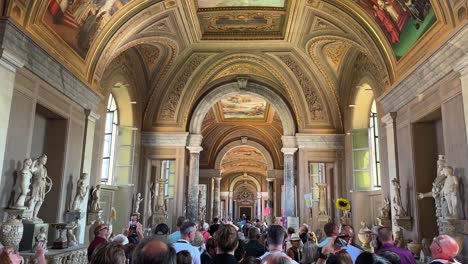 Tourists-walking-through-hallway-of-ancient-statues-and-artwork-in-Vatican-Museum,-Vatican-City,-Italy