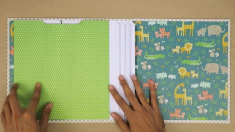 Creating-a-colorful-scrapbook-album-with-baby-animal-themed-pages-and-hands-placing-paper-sheets-inside