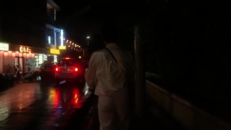 Person-in-white-coveralls-walking-down-a-rainy-city-street-at-night