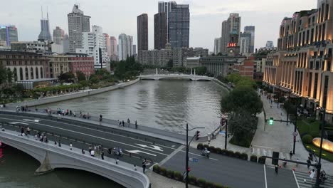 Traffic-and-pedestrians-cross-a-bridge-in-Shanghai-China,-skyscrapers-and-business-center-in-daylight-at-Huangpu-river