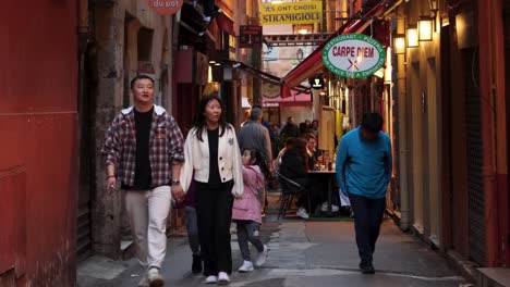 Asian-family-walks-by-restaurant-in-alley-in-old-town-of-Nice,-France,-static-view