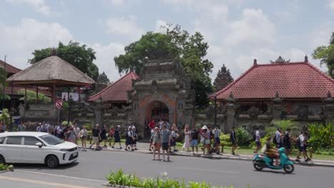 People-walking-on-a-busy-street,-in-front-of-the-famous-Ubud-Palace-of-Bali,-Indonesia,-sightseeing,-static-shot-and-copy-space