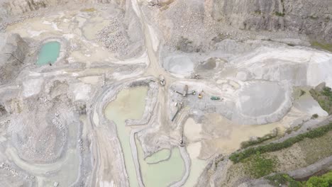 Aerial-view-of-an-earth-moving-team-working-at-the-bottom-of-an-aggregate-quarry,-showcasing-the-scale-of-operations-and-machinery