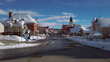 View-of-downtown-Leadville,-Colorado,-Mainstreet-Harrison-Avenue-with-traffic,-on-a-sunny-blue-skay-snowy-day-at-sunset