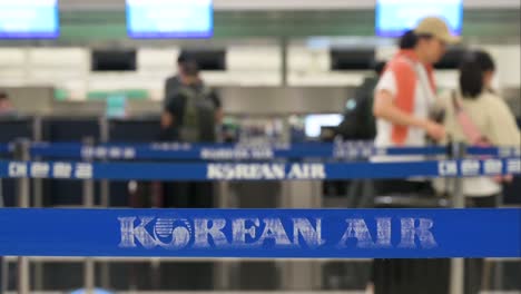 Los-Pasajeros-Hacen-Fila-Para-Registrarse-En-El-Aeropuerto-Internacional-De-Hong-Kong,-Donde-El-Logotipo-De-Korean-Air,-Que-Representa-A-La-Aerolínea-Más-Grande-Y-De-Bandera-De-Corea-Del-Sur,-Se-Exhibe-De-Manera-Prominente-En-Una-Cinta-De-Barrera.