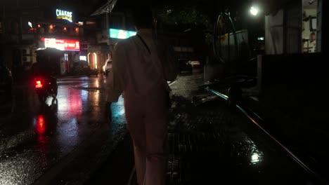 A-person-walks-with-an-umbrella-on-a-rainy-night,-neon-signs-illuminating-the-wet-street