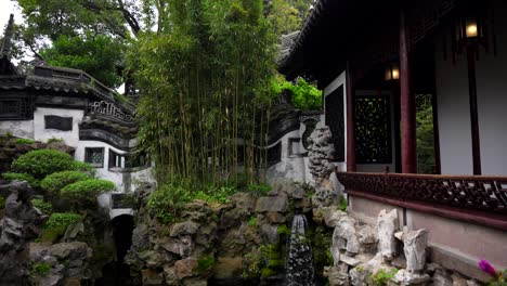 Bamboo-trees-and-small-artificial-waterfall-falling-into-a-pond-in-Yuyuan-Garden,-traditional-Chinese-architecture