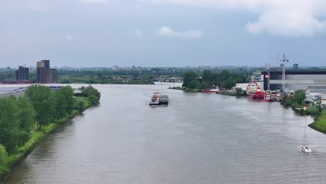 The-Vrido-Container-Ship-is-Making-Its-Way-Along-the-River-in-Alblasserdam,-South-Holland,-Netherlands---Drone-Flying-Forward