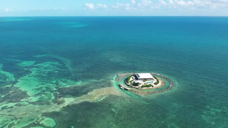 Aerial-view-of-East-Sister-Rock-Island-in-Florida,-surrounded-by-clear-turquoise-waters-and-coral-reefs-under-a-sunny-sky