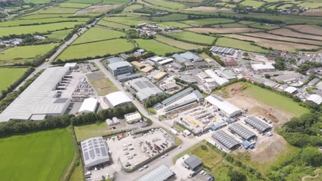 Drone-flyover-of-an-industrial-estate-featuring-non-descript-logistics-and-industrial-units,-highlighting-the-systematic-layout-of-warehouses,-loading-docks,-and-parking-areas-within-a-rural-landscape