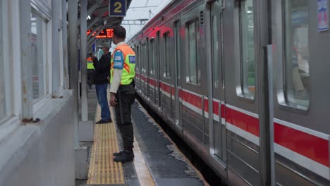 Guard-In-Uniform-On-The-Railway-Station-Platform-With-A-Train-Passing-To-Sudimara,-Tangerang-Selatan,-Indonesia