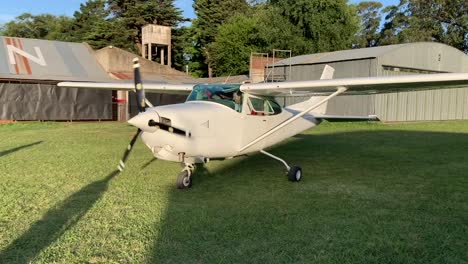 External-close-up-view-of-a-white-color-small-plane-starting-up-the-engine-over-a-green-grass-field