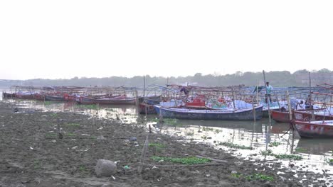 Boats-for-Pilgrims-at-sacred-Hindu-religious-site-Triveni-Sangam,-Dry-soil-in-summer-heat-wave-at-Ganga-river-shore-under-hazy-sky