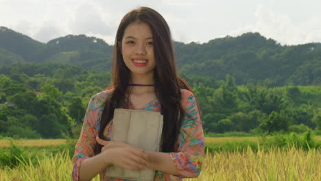 Joven-Estudiante-Que-Trabaja-En-Una-Plantación-De-Arroz-Usando-Una-Tableta-Sonriendo-Frente-A-La-Cámara-Con-Ropa-Agrícola-Tradicional-De-Vietnam