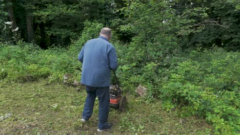 Man-trying-to-clear-heavily-overgrown-garden-brambles-using-a-mower,-highlighting-the-effort-in-a-rural-setting