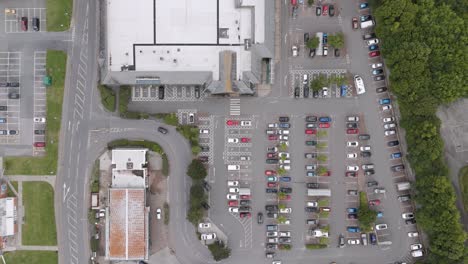 Aerial-fly-out-of-a-nondescript-UK-supermarket-and-carpark,-providing-a-broader-view-of-the-supermarket-complex,-parking-area,-and-nearby-facilities