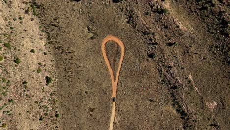 Vehicle-on-a-dusty-road,-drone-shot,-heading-to-a-vast-rocky-landscape,-dead-end-ahead-with-a-circle-in-the-road---outdoor-adventure-through-remote-rugged-wilderness