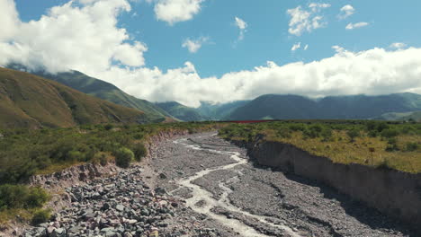 Drone-Avanzando-Sobre-Un-Río-De-Piedra-Casi-Seco-En-Jujuy-Cerca-De-La-Ruta-9-En-Un-Hermoso-Día-Soleado,-Con-La-Cordillera-De-Los-Andes-De-Fondo