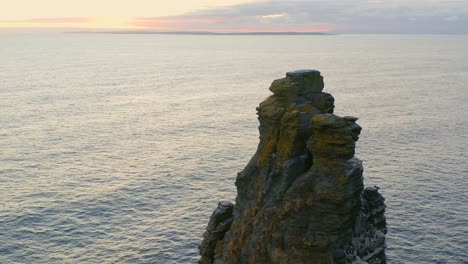 Slow-aerial-orbit-of-sea-stack-at-Cliffs-of-Moher,-featuring-puffins-and-seagulls,-with-vibrant-sunset-colors