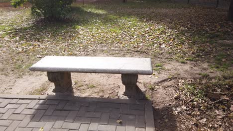 Closeup-of-a-bench,-long-stone-seat-in-autumn-garden,-midday-with-fallen-leaves