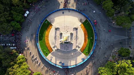 Overhead-drone-shot-of-Angel-of-Independence-victory-column-monument-on-a-roundabout-on-Paseo-de-la-Reforma-Avenue-street,-Day-of-the-Dead-parade-celebration-in-downtown-Mexico