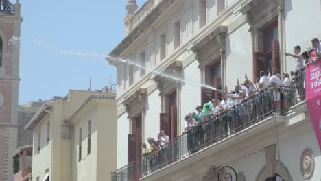 People-on-a-balcony-with-a-hose-spraying-water-on-spectators-at-a-cultural-event-with-a-yellow-ball-in-the-air-in-Sagunto