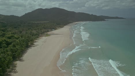 Young-caucasian-woman-walks-on-empty-tropical-beach,-forward-aerial