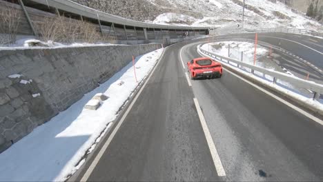 Following-a-ferrari-around-a-corner-on-a-mountain-road-with-snow-and-mountain-architecture