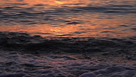 Sea-waves-gently-splash-on-the-coastline-at-Batumi,-Georgia,-with-evening-hues-reflecting-on-them-as-the-sun-sets-on-the-horizon,-showcasing-the-serene-beauty-of-coastal-twilight