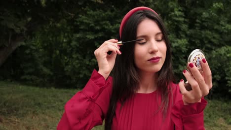 Pretty-girl-in-red-draws-eyelashes-in-park