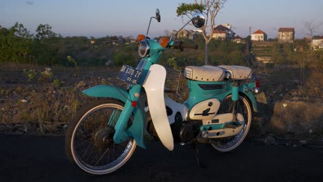 Vintage-classic-Honda-C70-motorcycle-in-turquoise-and-white-color-parked-outdoors-at-sunset