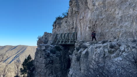 Joven-Excursionista-Con-Mochila-Pasando-Por-Una-Pasarela-De-Madera-En-Una-Ruta-De-Senderismo-En-Las-Montañas-De-Guadalupe,-Texas,-EE.UU.