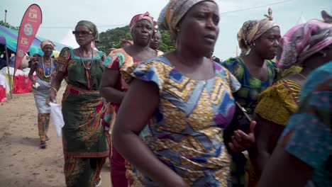 Women-dance-past-the-camera,-singing-and-waving-white-handkerchiefs-and-flags-in-a-festival-celebration-in-Ghana,-West-Africa