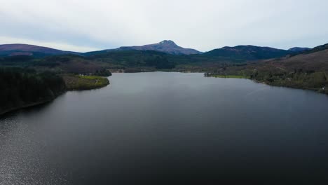 Vista-Aérea-Sobrevolando-Las-Aguas-Del-Lago-Ard-Con-La-Montaña-Ben-Lomond-En-La-Distancia