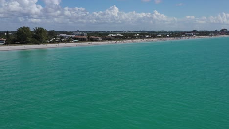 Luftaufnahme-Eines-Sonnigen-Strandes-In-Florida-Mit-Einem-Vogel,-Der-über-Türkisfarbenes-Wasser,-Sandstrand-Und-Entspannende-Strandbesucher-Fliegt