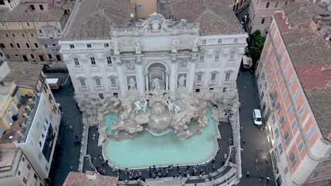 Aerial-descending-down-over-Trevi-Fountain-and-city,-Rome-Italy-landmark-at-sunrise