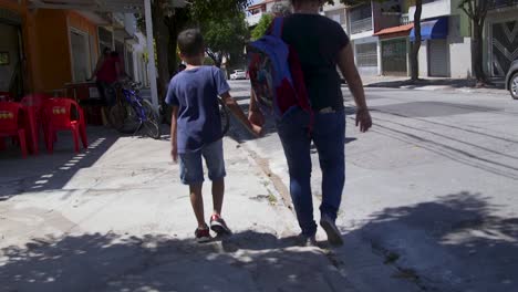 Young-boy-holding-his-mother's-hand-while-walking-in-the-street