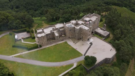 Aerial-fly-up-view-of-Castle-Drogo-surrounded-by-greenery-in-Devon,-UK,-July-2024