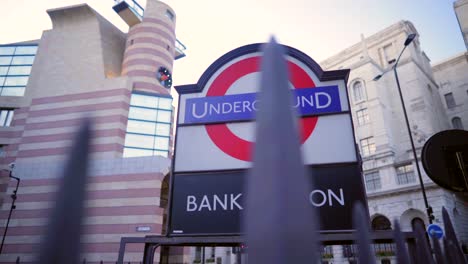 Bank-Station-underground-entrance-sign-in-downtown-London,-stone-city-buildings,-and-blue-sky-with-light-clouds