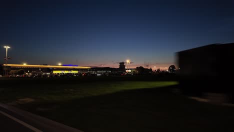 Pov-footage-of-leaving-Riga-International-Airport-by-car-during-twilight,-capturing-the-night-lights-and-skyline