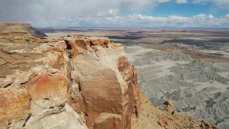 Vista-Aérea-De-Una-Mujer-Joven-Caminando-En-La-Cima-De-Una-Mesa-Cerca-De-Un-Acantilado-Sobre-Las-Tierras-Baldías-Del-Desierto,-Toma-Con-Dron