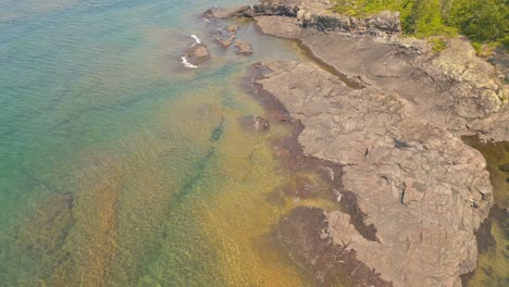 Aerial-drone-footage-of-clear-coastal-waters-with-rocky-formations-and-lush-shoreline