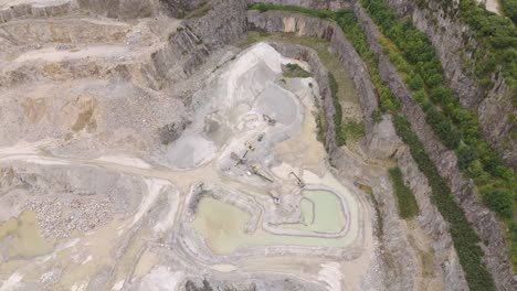 Large-machinery-moving-earth-at-the-bottom-of-an-aggregate-quarry,-capturing-the-heavy-equipment-in-action