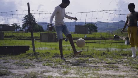 Dos-Niños-Jugando-Al-Fútbol-En-Un-Pueblo-Rural-Sudafricano-Con-Una-Valla-De-Alambre-Como-Portería