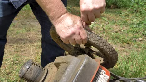 Caucasian-man-attempting-to-remove-garden-debris-from-mower-wheel