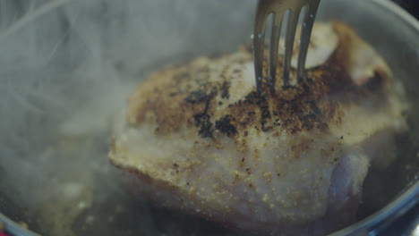 Beautiful-slow-motion-shot-flipping-a-piece-of-chicken-with-a-fork-inside-a-black-frying-pan-with-oil-and-smoke