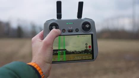 Close-up-of-a-person-holding-a-drone-controller-with-LCD-information-display-in-an-outdoor-field-setting