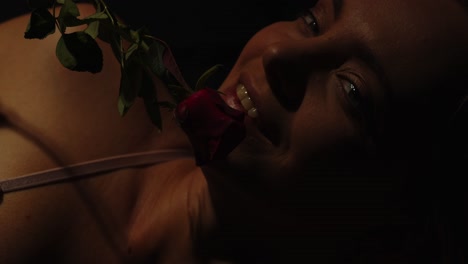 Close-up-of-a-beautiful-young-woman-smiling-while-a-red-rose-caresses-her-face