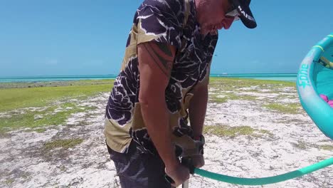 Hombre-Inflando-Equipo-De-Kitesurf-Y-Mujer-Parada-Con-Cometa-En-La-Playa,-Isla-Vapor-Los-Roques