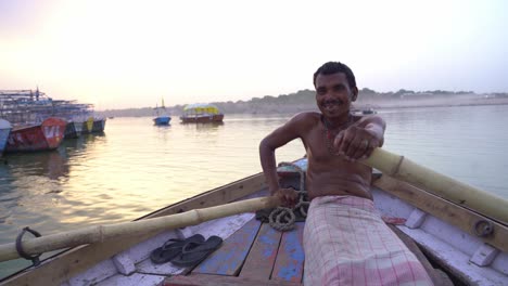 A-local-Indian-fisherman-with-bare-body-sailing-traditional-wooden-boat-in-Ganga-river-Triveni-Sangam-for-fishing-in-evening,-confluence-of-the-Ganges,-Yamuna,-and-Saraswati-River